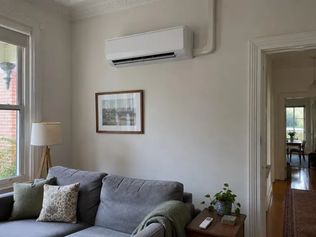 Clean split system on a living room wall above a sofa, with open louvre and cream walls in Norwood